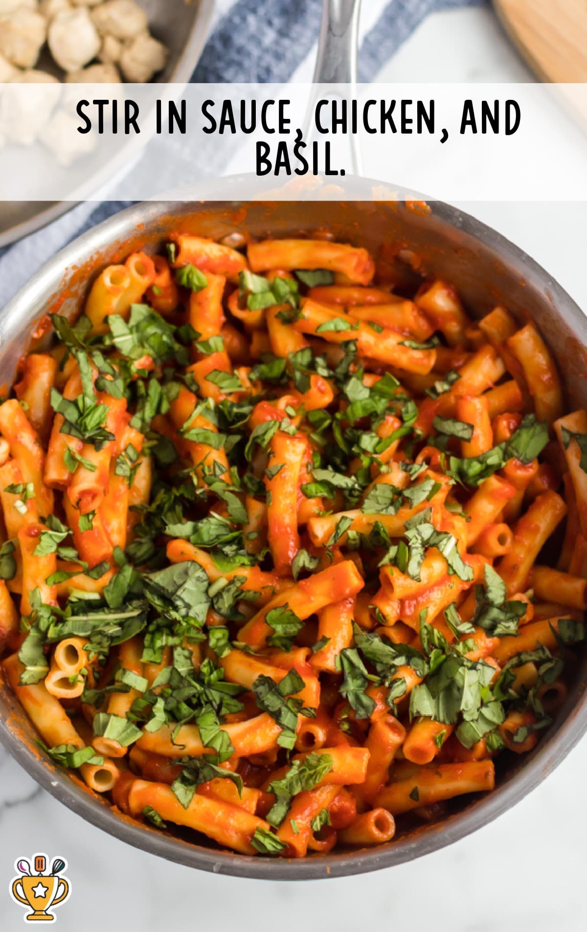 Cooked ziti pasta tossed with tomato sauce, chopped cooked chicken, and fresh basil in a stainless steel skillet.