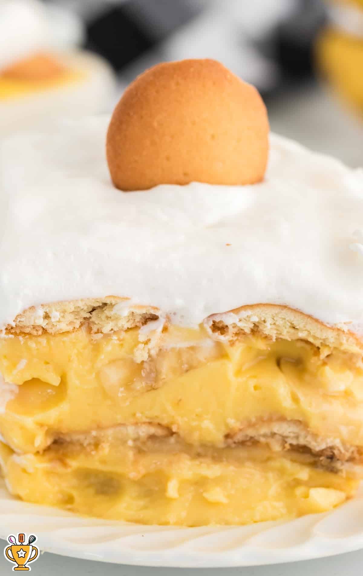 Close-up view of banana pudding slice with whipped topping and a single Nilla wafer on top, showing creamy pudding and cookie layers on a white plate.