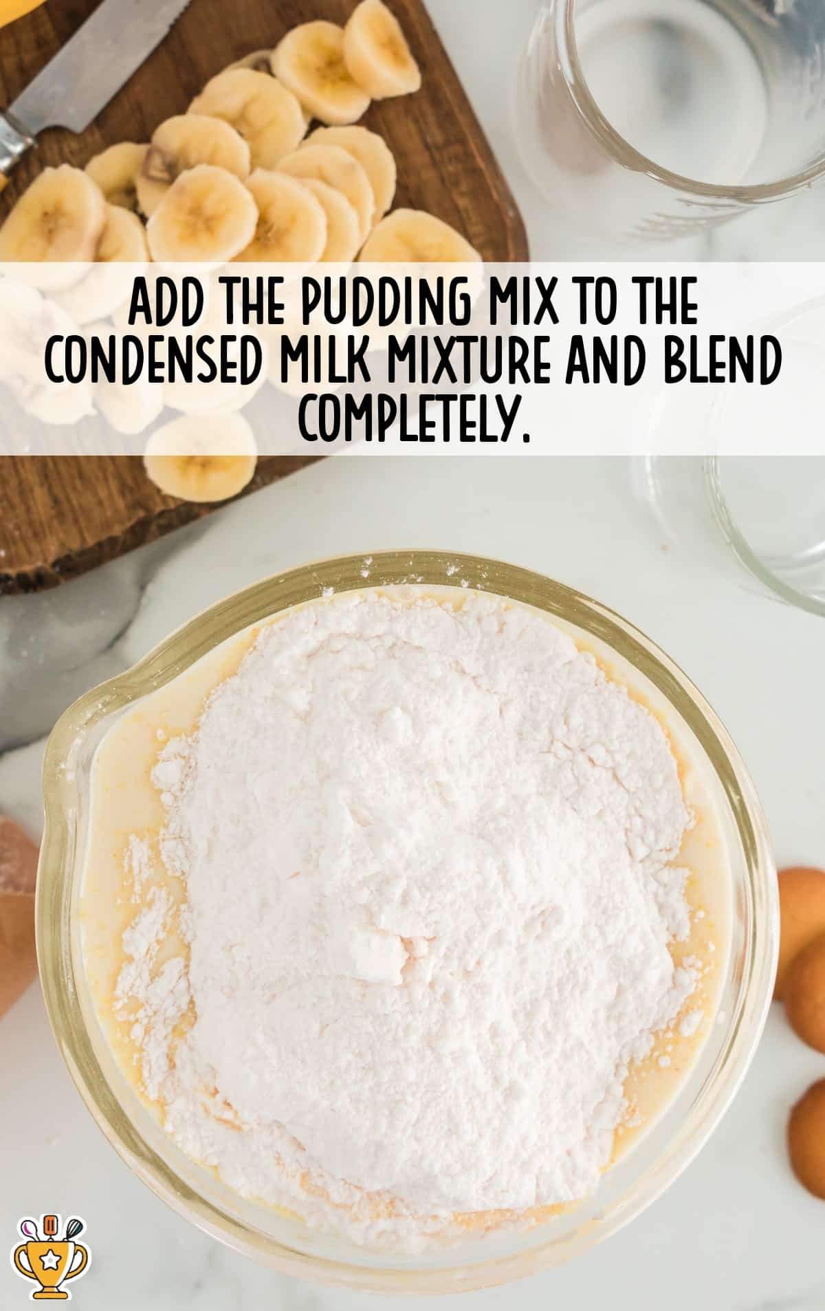 Overhead shot showing pudding mix being added to condensed milk in a mixing bowl on a marble countertop with sliced bananas and other ingredients nearby.