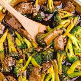 Overhead shot of beef and broccoli stir fry in a skillet with a wooden spoon, surrounded by green onions.