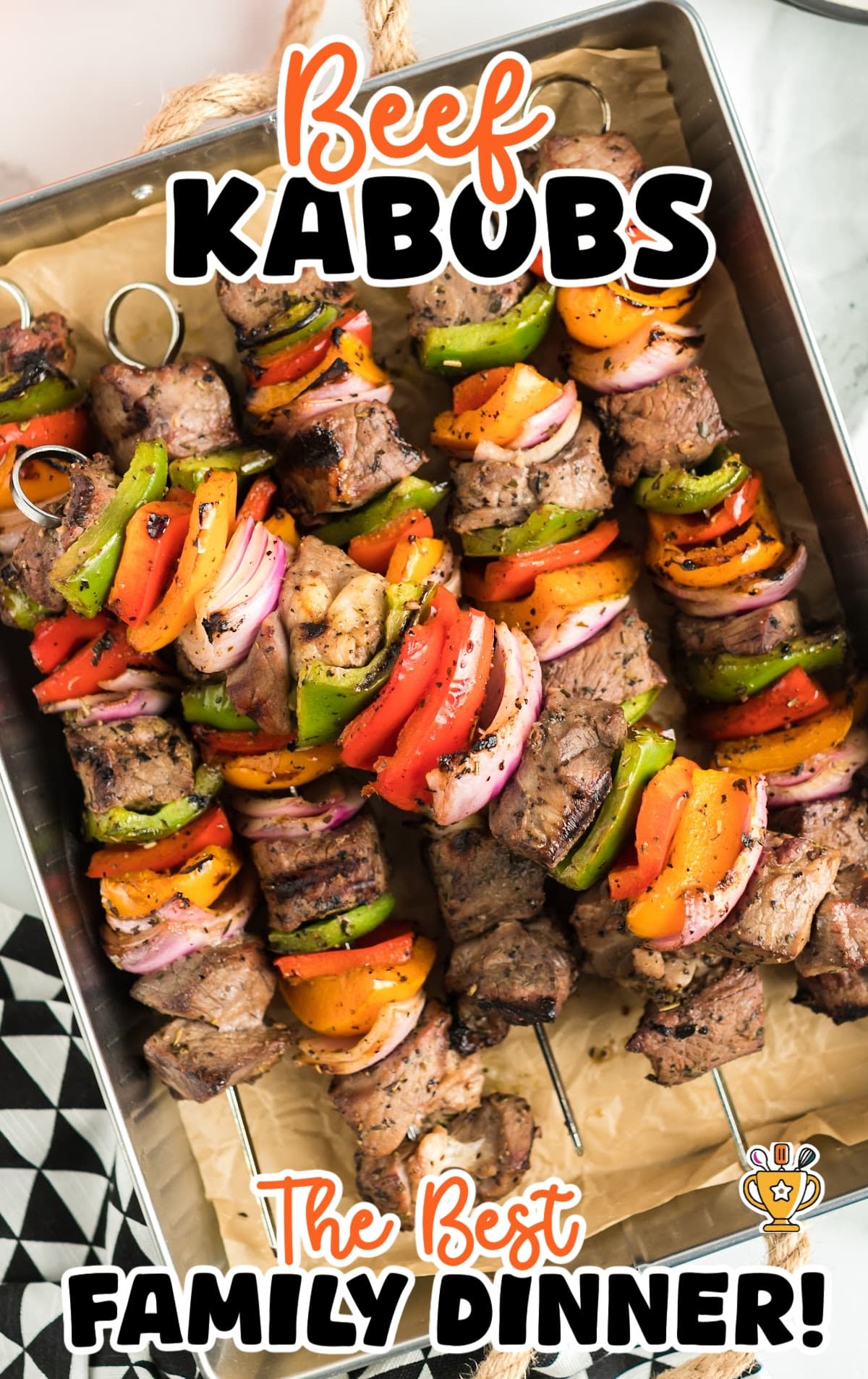 Close-up of grilled beef kabobs in a tray, stacked with red onions, peppers, and juicy grilled beef chunks.