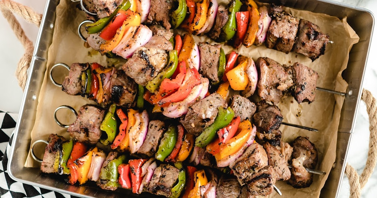 Repeated close-up of beef kabobs layered with grilled peppers and onions in a serving tray.
