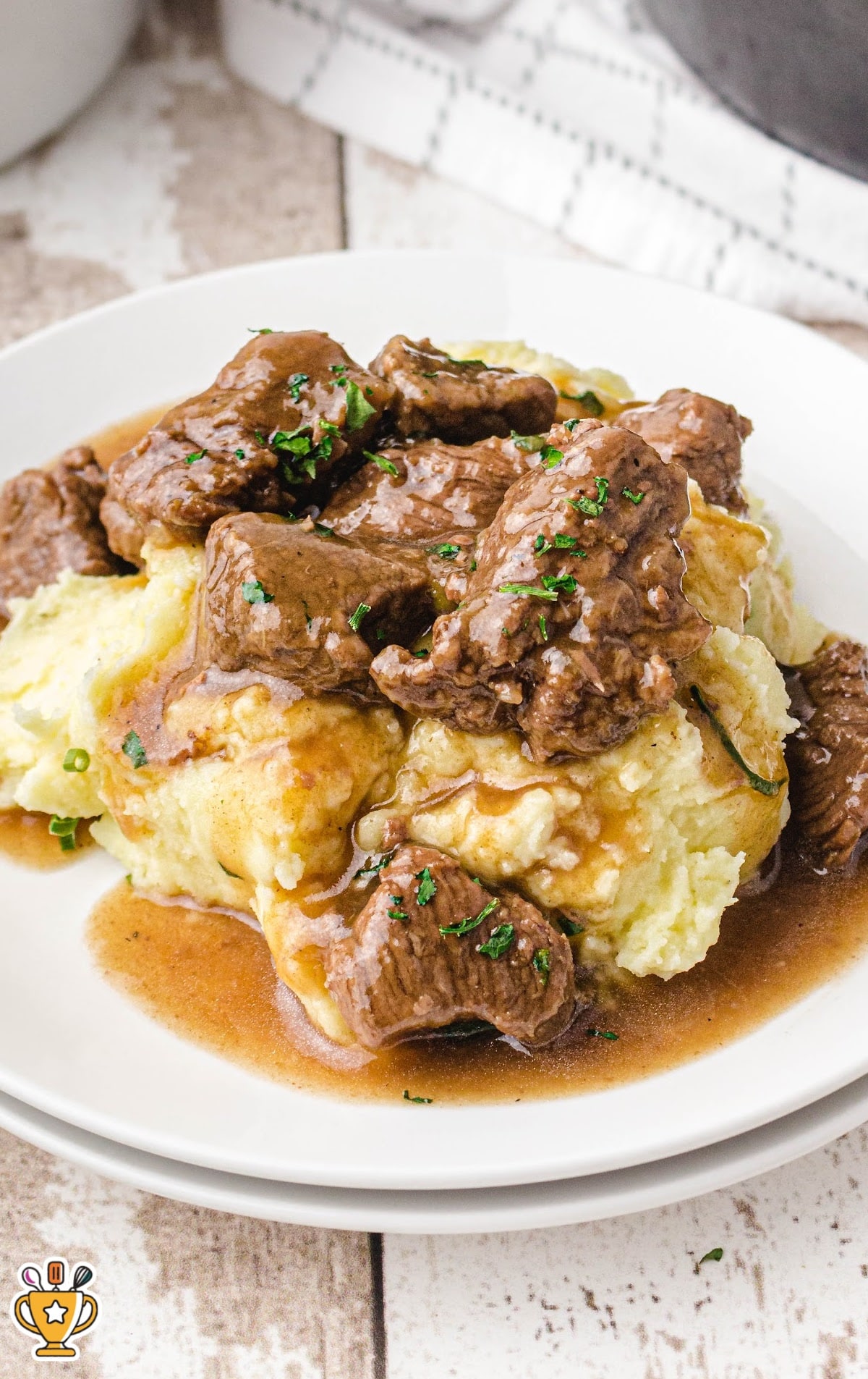Beef tips with gravy served on a plate of mashed potatoes with gravy pooling around the edges.