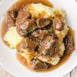 Overhead close-up of beef tips and gravy on top of creamy mashed potatoes, garnished with parsley.