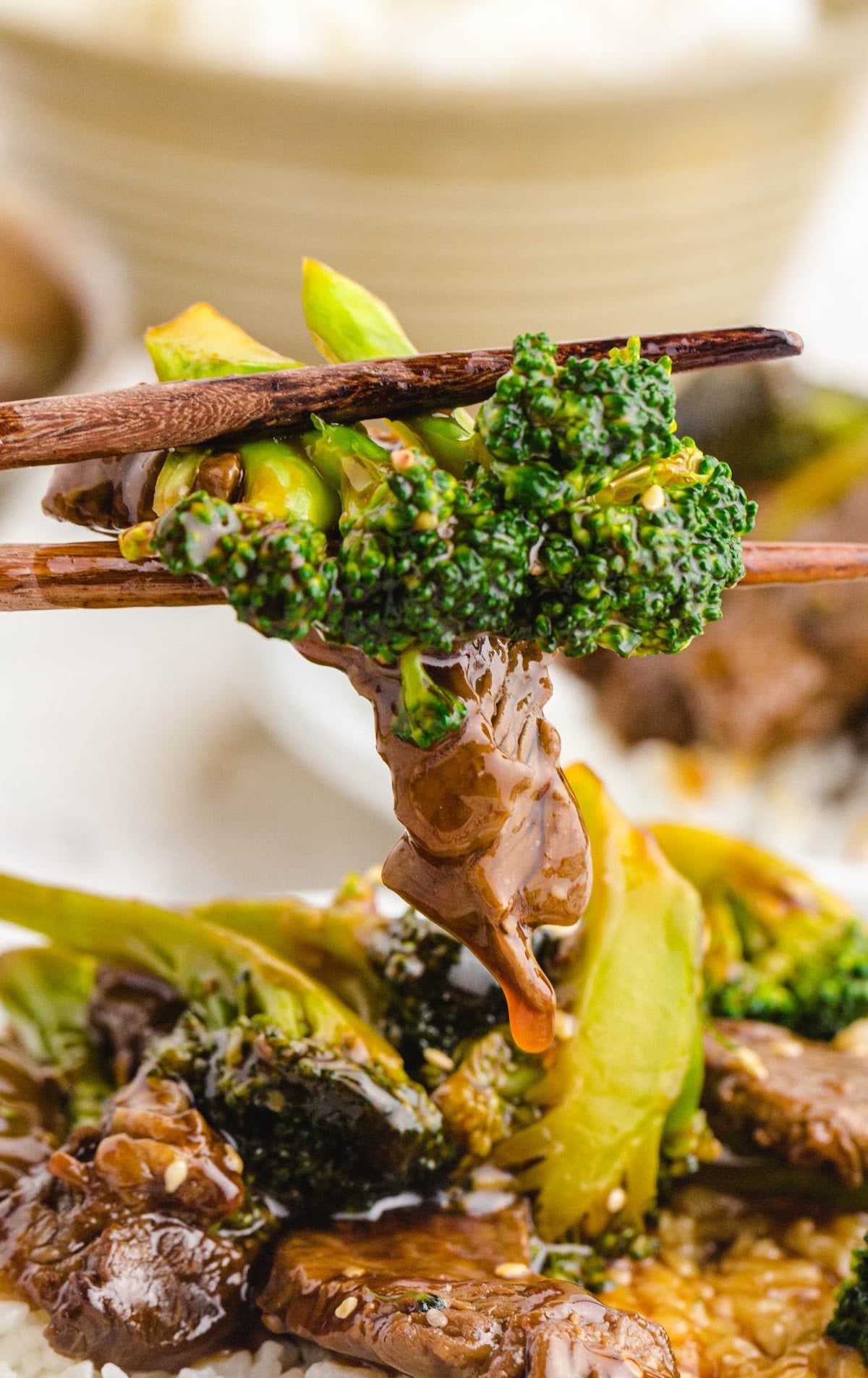Close-up of chopsticks holding a bite of beef and broccoli with saucy rice in the background.