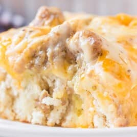 Close-up of a fluffy slice of biscuits and gravy breakfast casserole, loaded with melted cheddar and sausage.