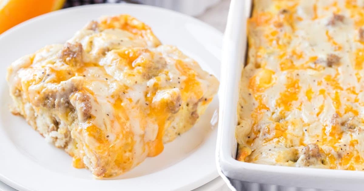 One serving of cheesy biscuits and gravy breakfast casserole on a plate beside a full baking dish of the casserole.