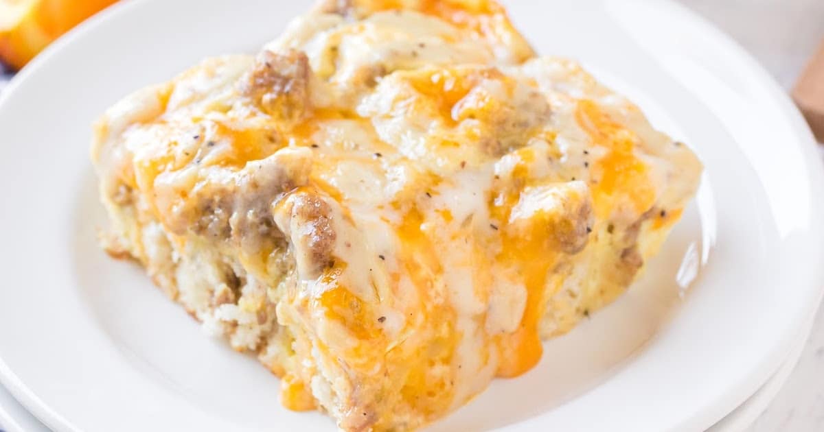 Overhead shot of a single slice of biscuits and gravy breakfast casserole served on a white plate, showing off melted cheese.