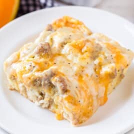 Top-down view of a plate with one cheesy, golden slice of biscuits and gravy casserole on a white background.