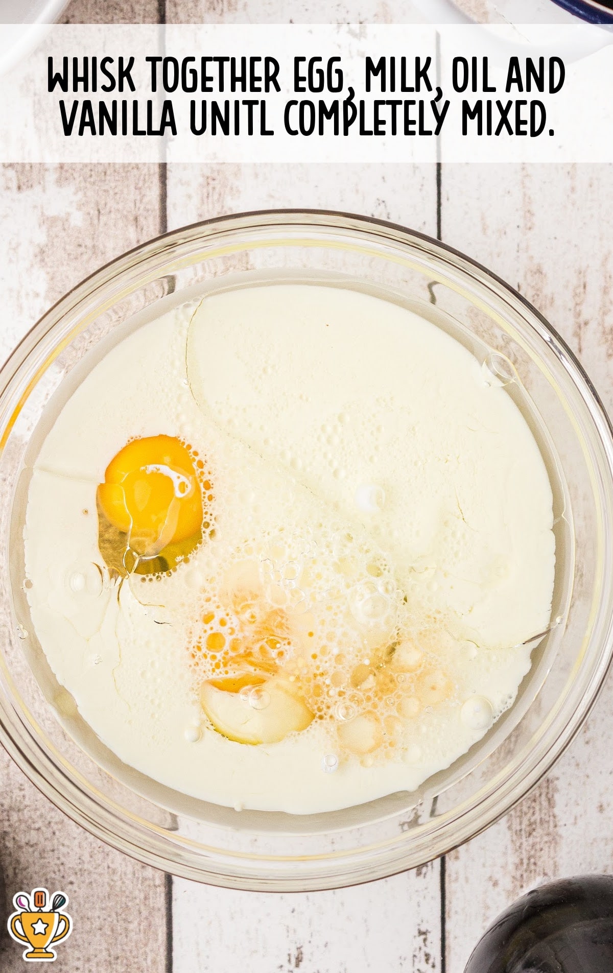Mixing bowl with egg, milk, oil, and vanilla before whisking, shown with step instructions on combining ingredients