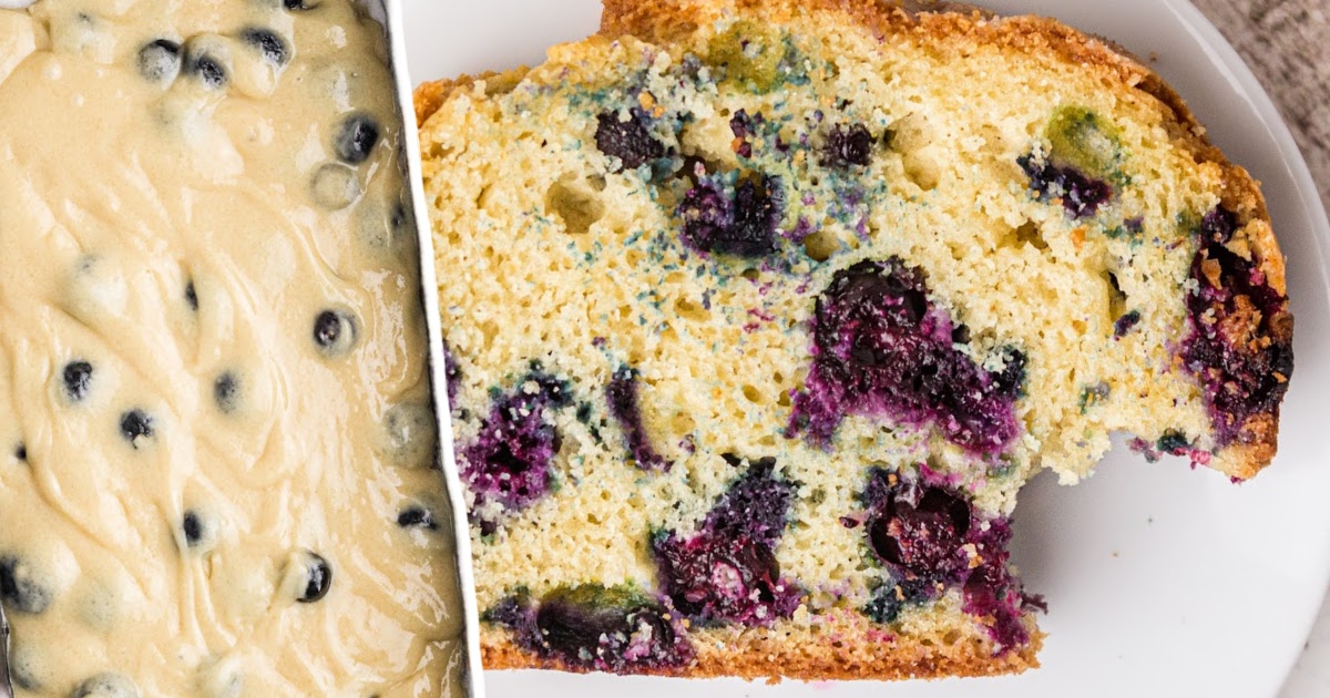 Sliced blueberry bread stacked on a white plate beside a glass bowl filled with floured fresh blueberries.