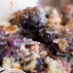 Close-up of a blueberry cobbler served with vanilla ice cream, topped with cinnamon and a side of fresh blueberries in a bowl. Text overlay says "Blueberry Cobbler With Only 5 Ingredients!"