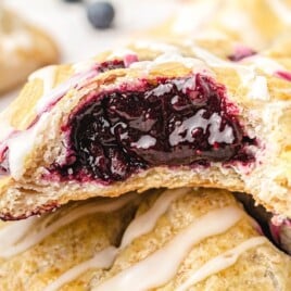 Close-up view of a golden blueberry hand pie broken open, showing a rich, glossy blueberry filling inside.