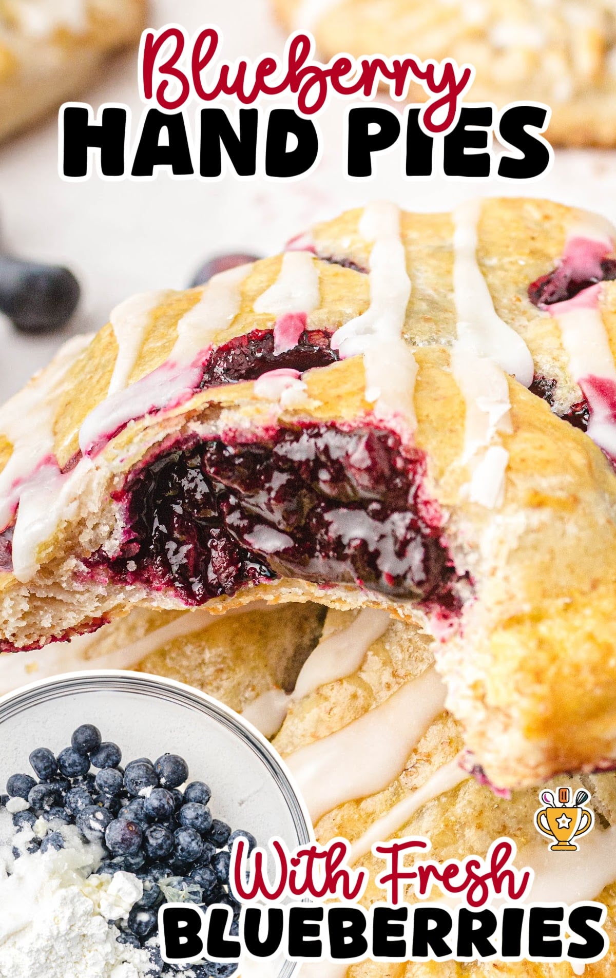 Blueberry hand pies stacked on parchment paper, drizzled with white icing and filled with a thick blueberry filling.