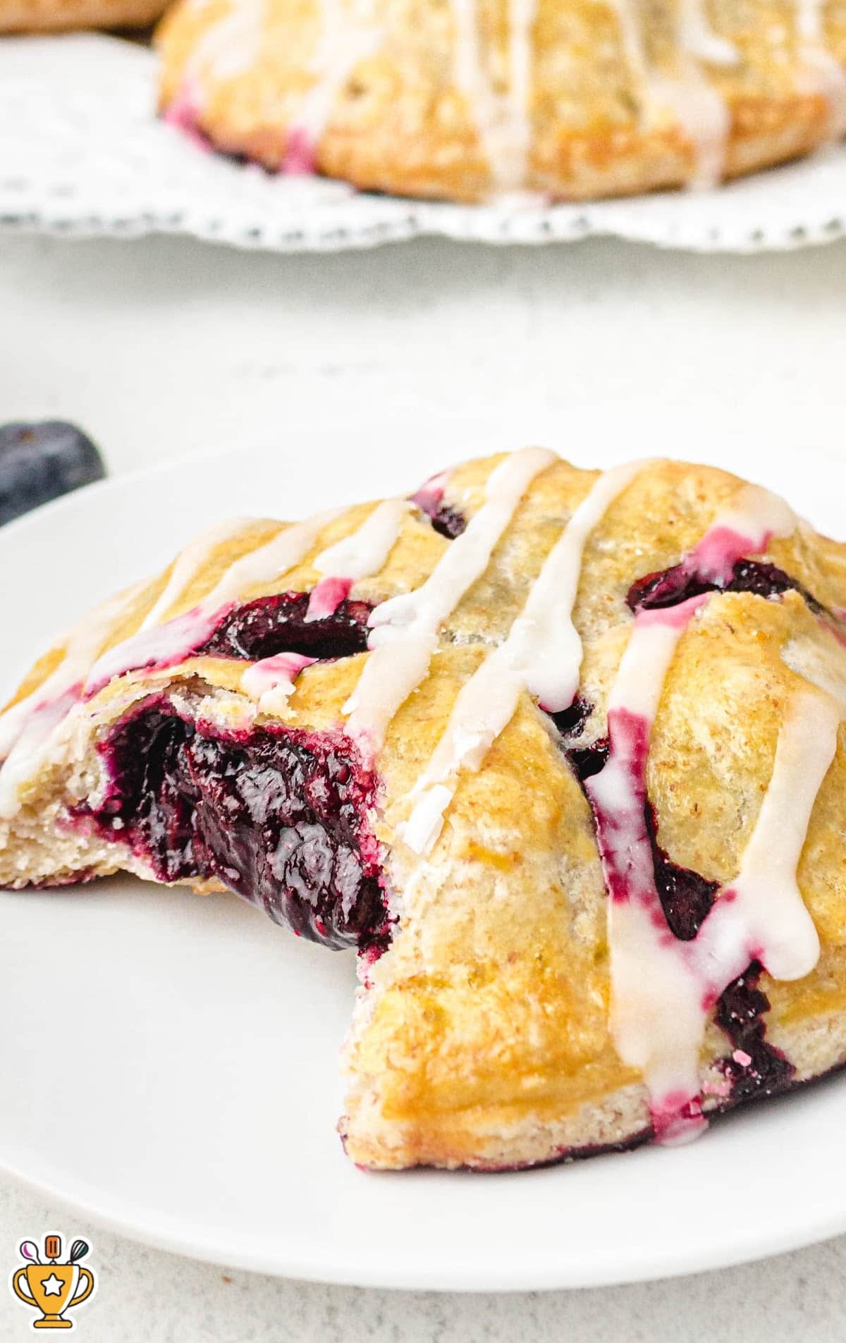 Single blueberry hand pie on a white plate, broken open to reveal a juicy, glossy blueberry filling with icing on top.