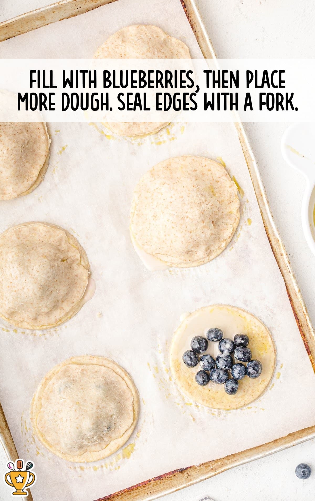 Fresh blueberries placed on pie dough circles before being topped with another layer and sealed with a fork.