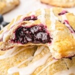 Close-up of blueberry hand pies on a baking tray with golden crusts and a white glaze drizzled over the tops.