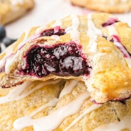 Close-up of blueberry hand pies on a baking tray with golden crusts and a white glaze drizzled over the tops.