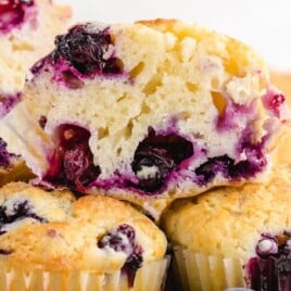 Golden blueberry muffins with a halved muffin on top displaying the juicy, baked-in berries and fluffy inside.