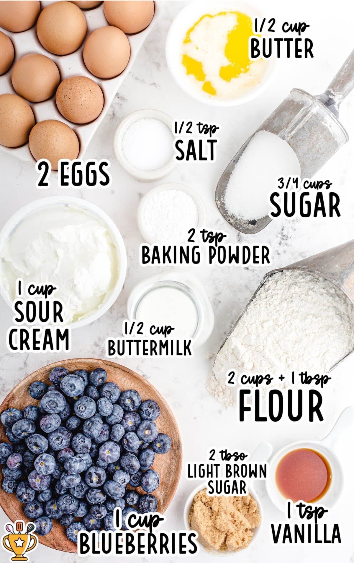 Overhead photo of labeled ingredients for blueberry muffins including eggs, butter, sour cream, blueberries, and flour.