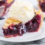 Slice of blueberry pie topped with a large scoop of vanilla ice cream, melting slightly onto the pie slice.