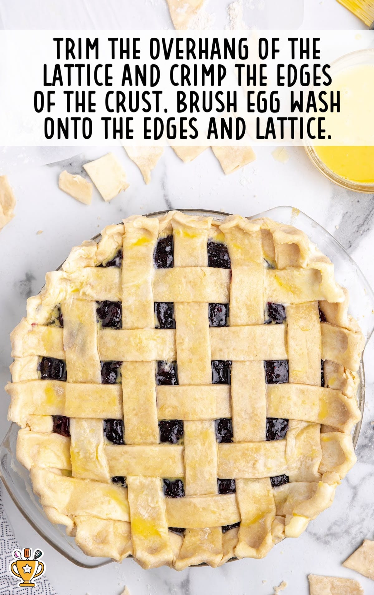 Fully latticed blueberry pie brushed with egg wash, ready for baking, with crimped edges and pie crust scraps around it.