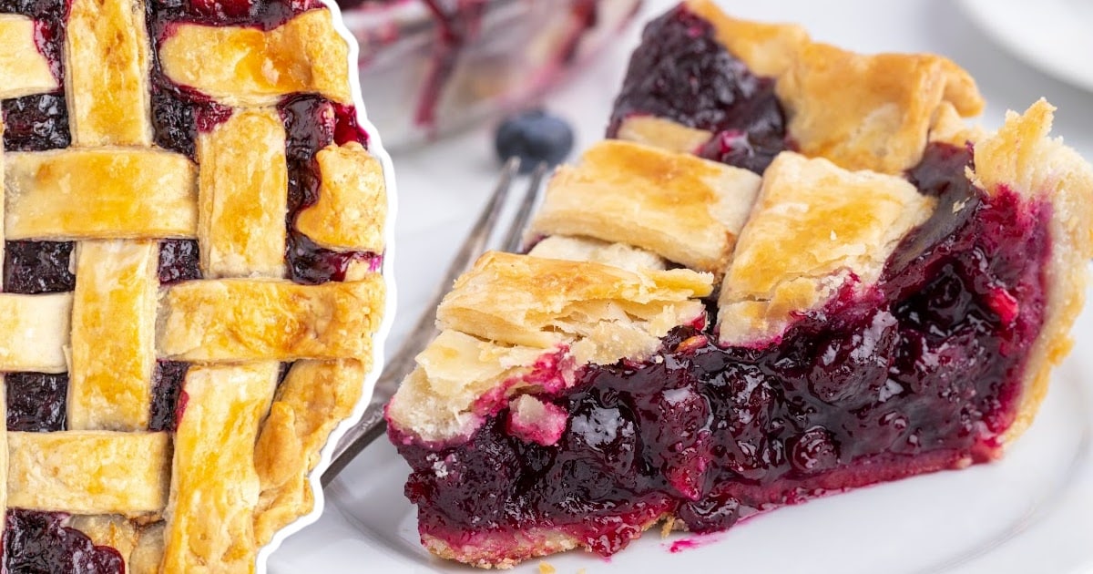Close-up showing half a whole lattice-topped blueberry pie and a slice of pie served on a white plate.