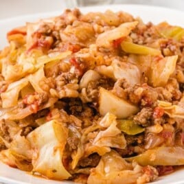 Close-up of a serving of cabbage roll casserole on a white plate with visible chunks of cabbage, rice, ground beef, and tomato sauce.