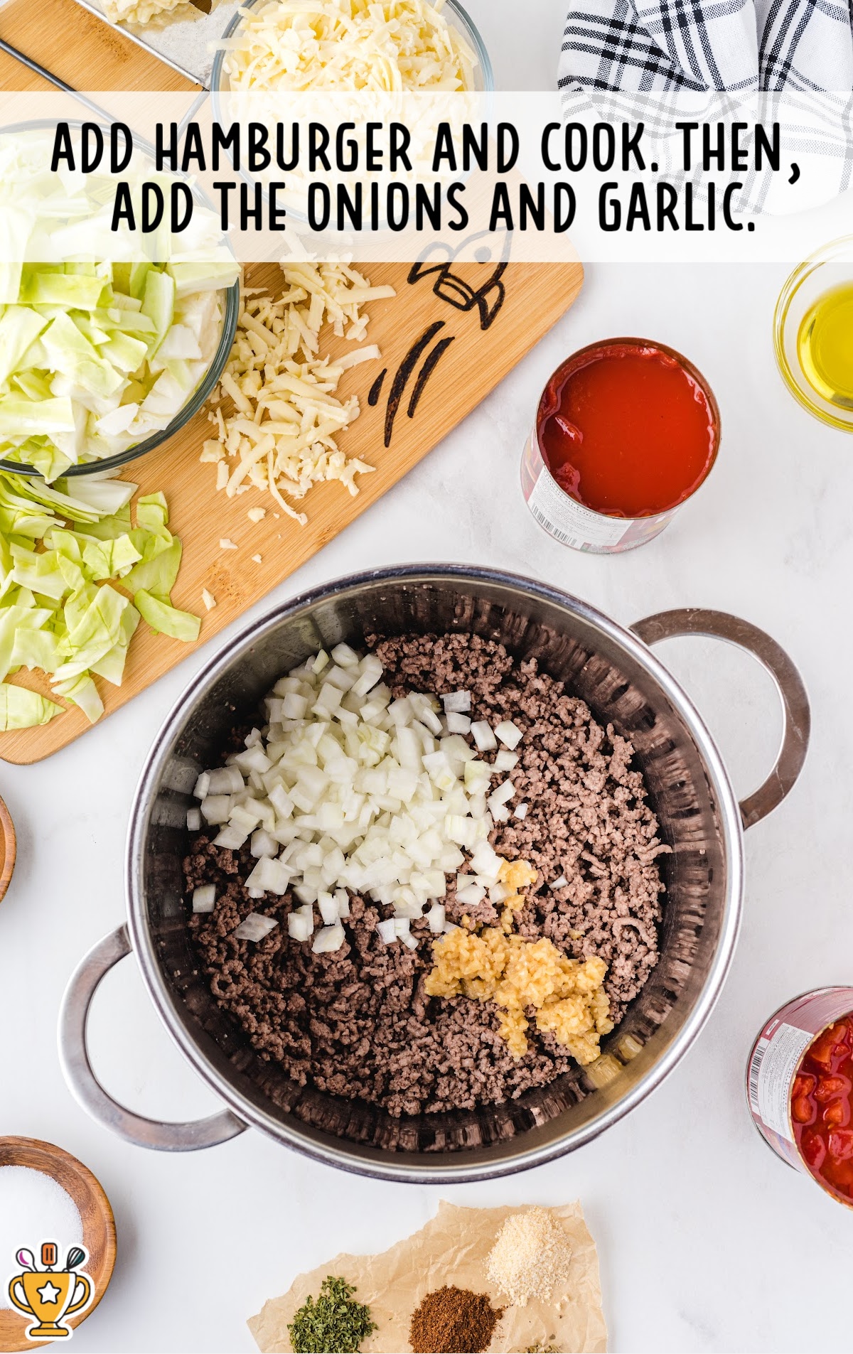 Ground beef cooking in a pot with freshly chopped onions and minced garlic, surrounded by shredded cheese and chopped cabbage.