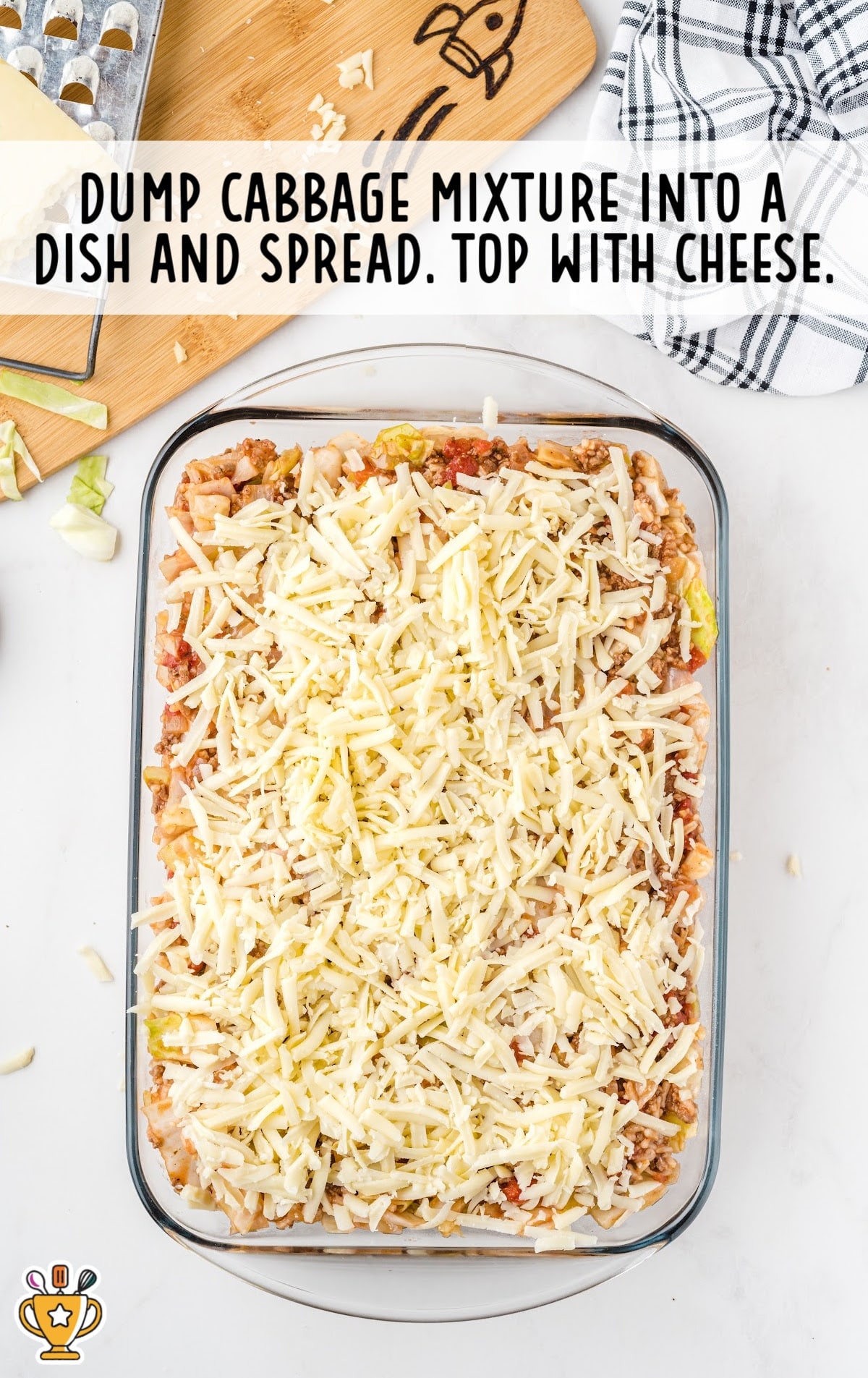 Unbaked cabbage roll casserole mixture spread in a glass baking dish and topped generously with shredded cheese.