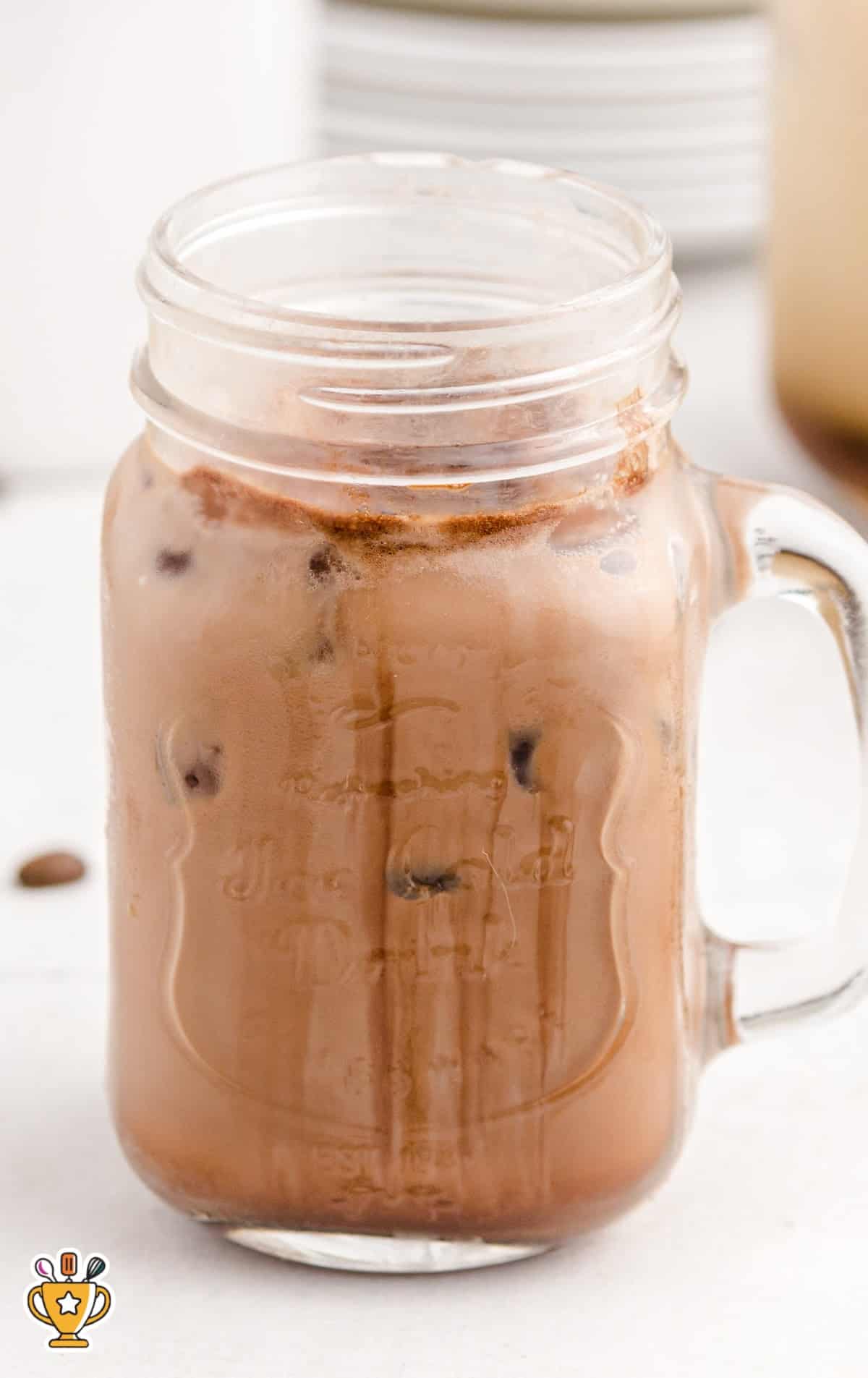 Tall mason jar filled with a chocolate-tinted iced caramel macchiato, condensation forming on the outside of the glass.