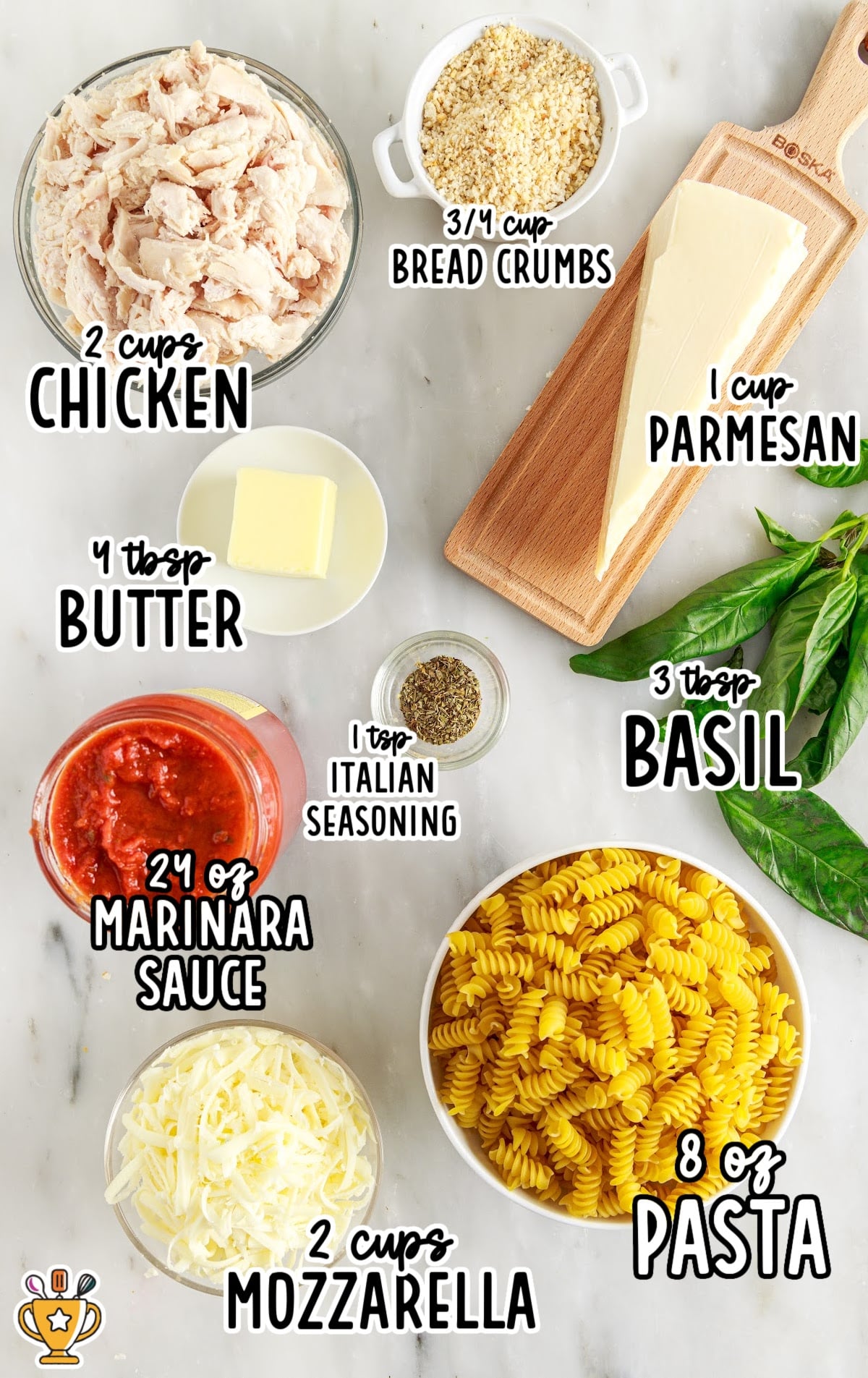 Flat lay of casserole ingredients: shredded chicken, dry rotini pasta, marinara sauce, shredded mozzarella, Parmesan wedge, breadcrumbs, butter, Italian seasoning, and fresh basil.