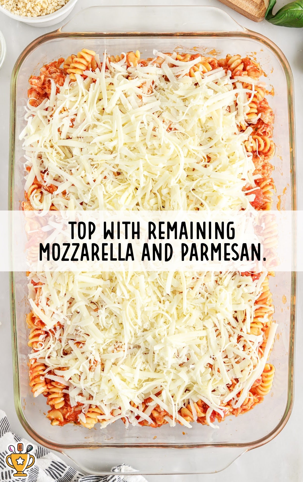 Pasta casserole topped with a thick layer of shredded mozzarella and parmesan cheese, ready for breadcrumb topping.
