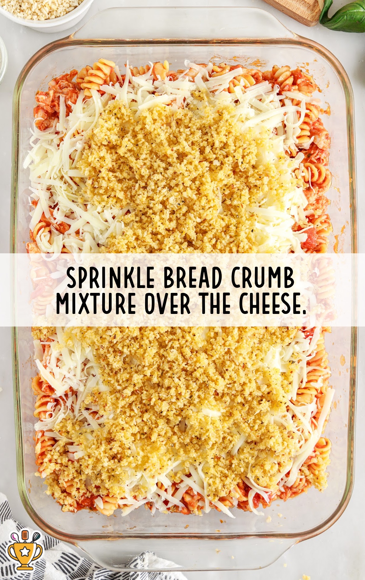 Unbaked casserole dish topped with golden seasoned breadcrumbs over a layer of shredded cheese and pasta.