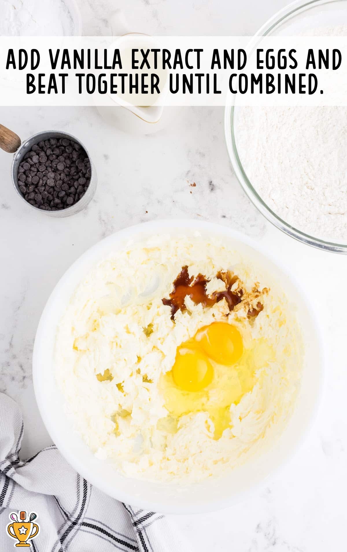 Mixing bowl with creamed butter and cream cheese mixture topped with vanilla extract and two cracked eggs.