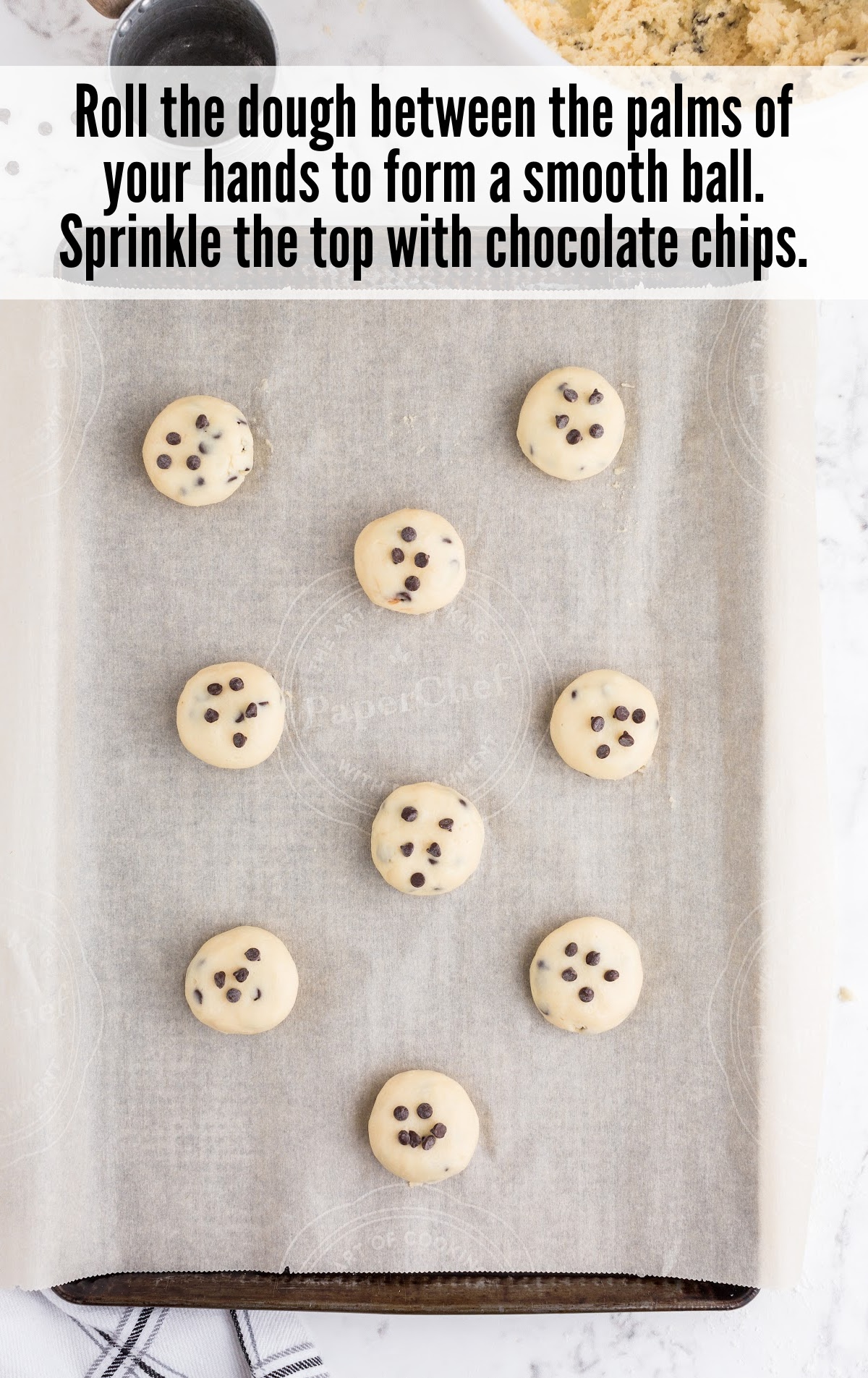 Raw cookie dough balls sprinkled with mini chocolate chips, placed evenly on a parchment-lined baking sheet.