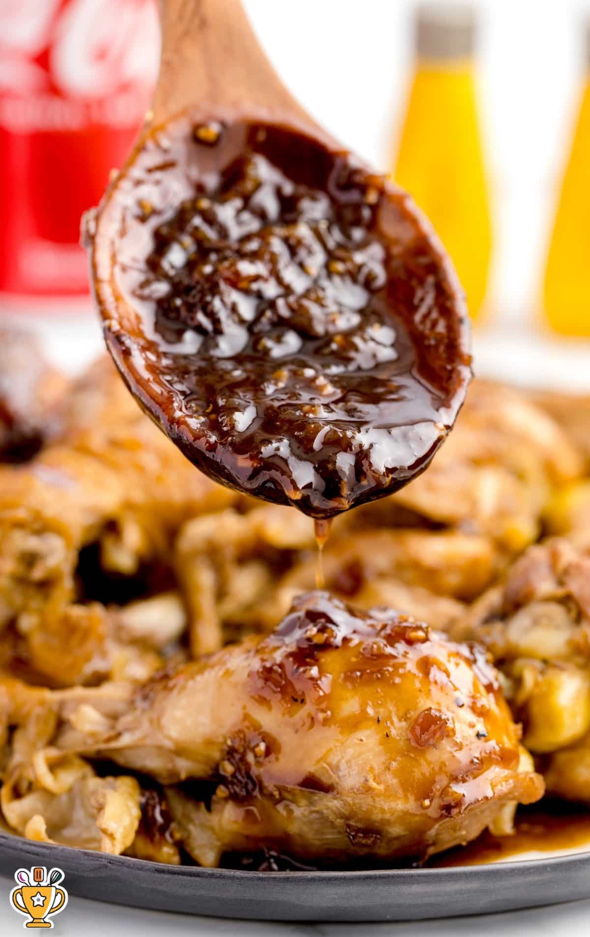 Wooden spoon drizzling thick Coca-Cola sauce over a piece of juicy chicken, with sauce clinging to the spoon.