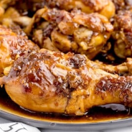 Close-up of glazed Coca-Cola chicken drumsticks on a white plate, coated in a sticky, rich brown sauce.