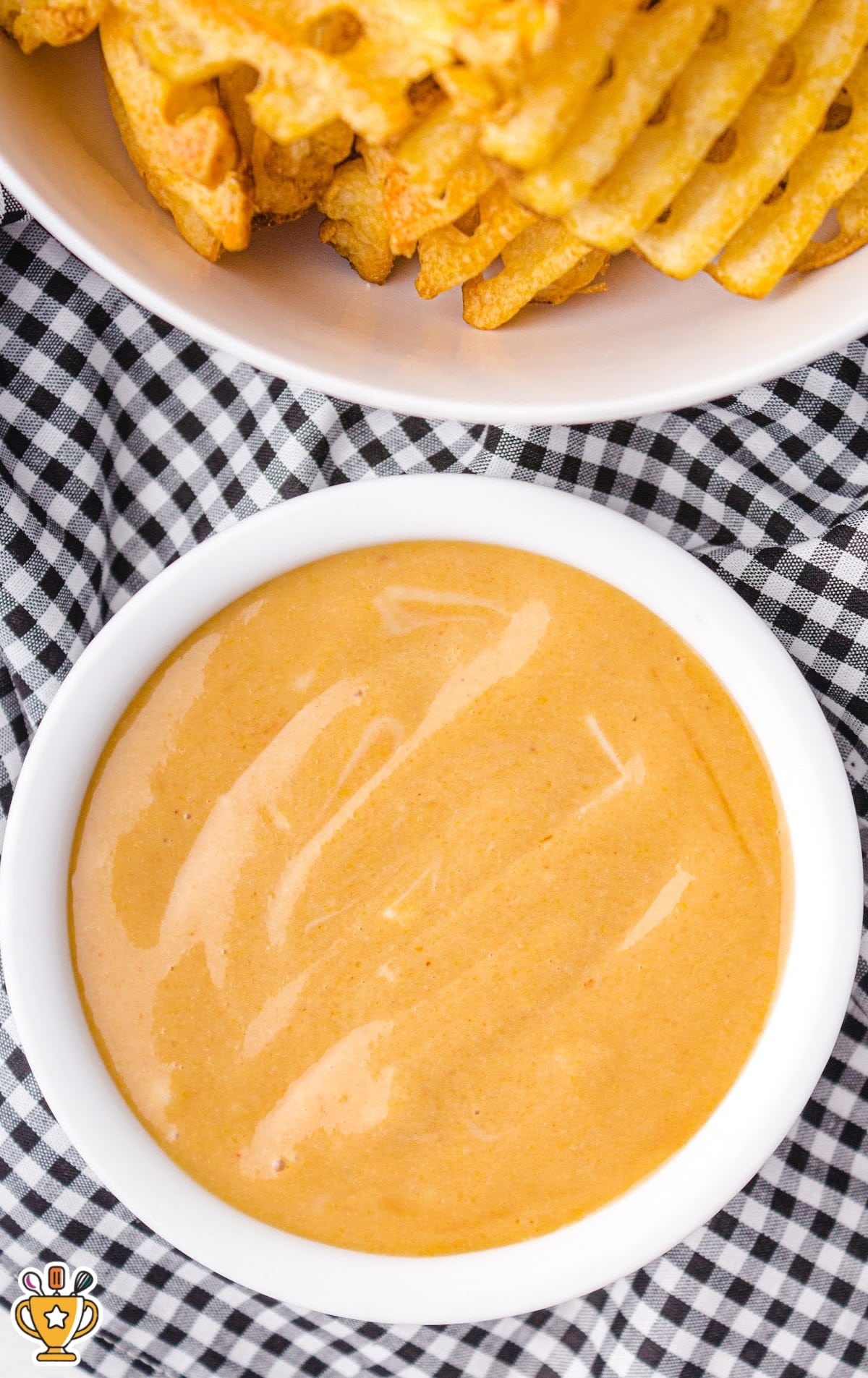 Bowl of homemade copycat Chick-fil-A sauce next to crispy waffle fries on a black-and-white checkered cloth.