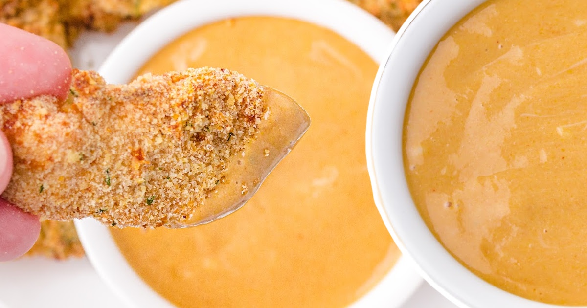 Hand dipping a crispy chicken tender into a smooth bowl of copycat Chick-fil-A sauce with another sauce bowl in view.