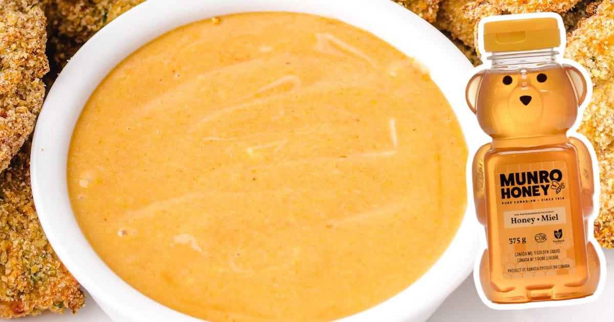 Close-up of a bowl of creamy copycat Chick-fil-A sauce with a honey bear bottle on the side and tenders in the background.