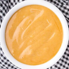 Bowl of homemade copycat Chick-fil-A sauce surrounded by waffle fries and tenders with ingredient images labeled on the bottom.
