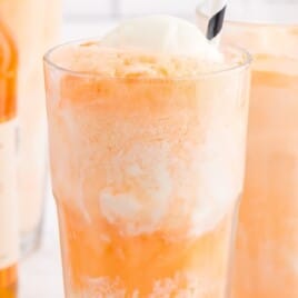 A creamy orange float with vanilla ice cream and a striped straw, placed in front of bottles of orange soda.