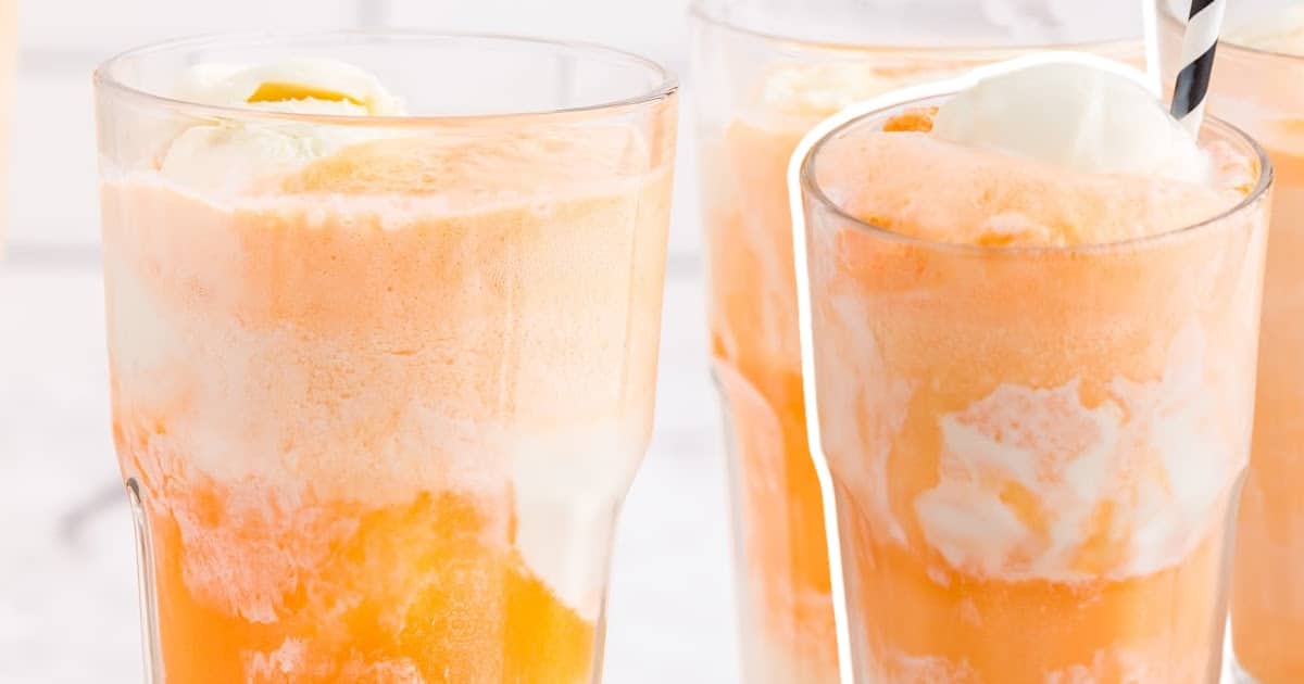 Four tall glasses of orange and vanilla creamsicle floats lined up, with visible scoops of vanilla ice cream floating on top.