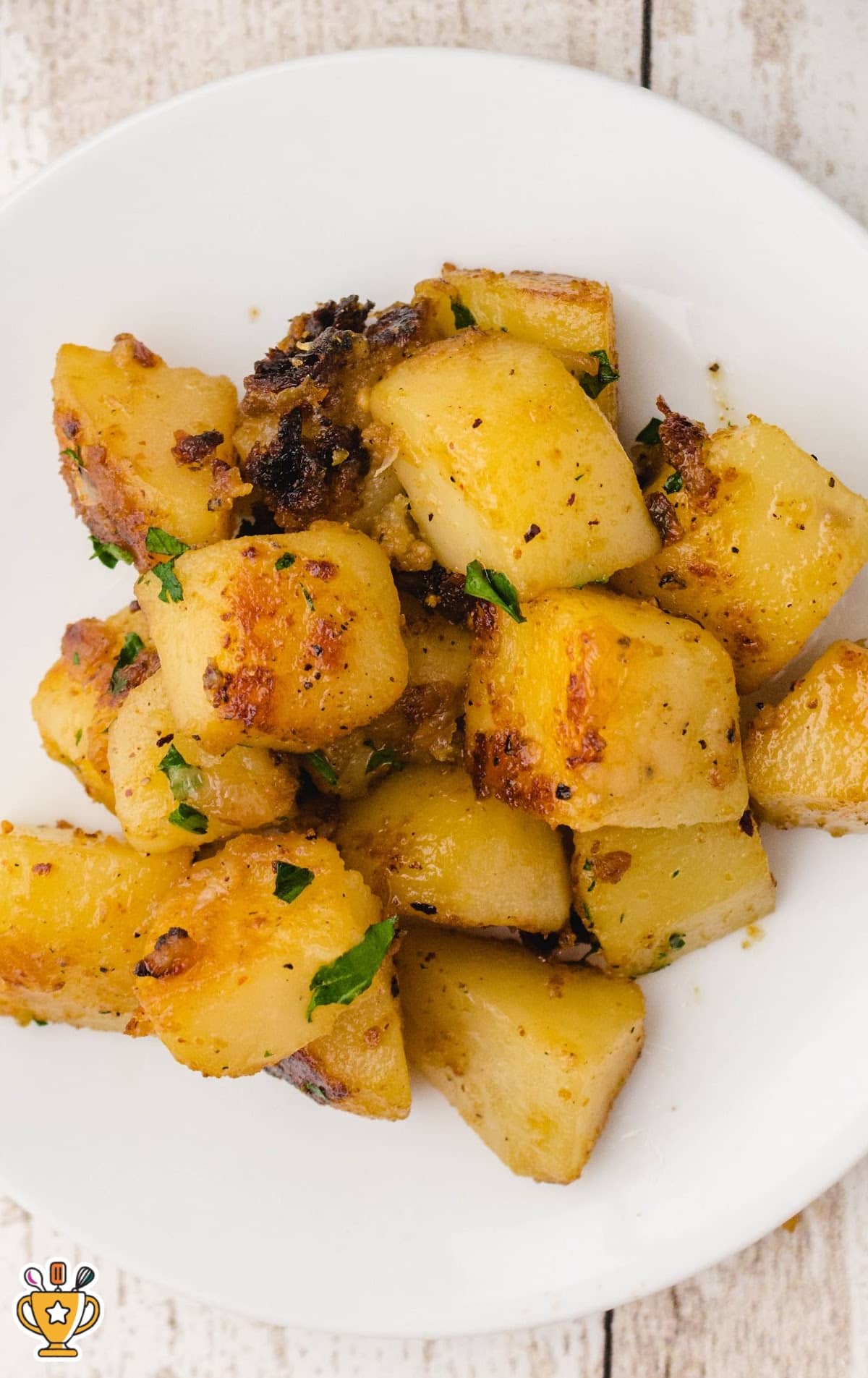 Close-up of a white plate filled with crispy, golden-brown potatoes garnished with parsley, showcasing texture and caramelization.