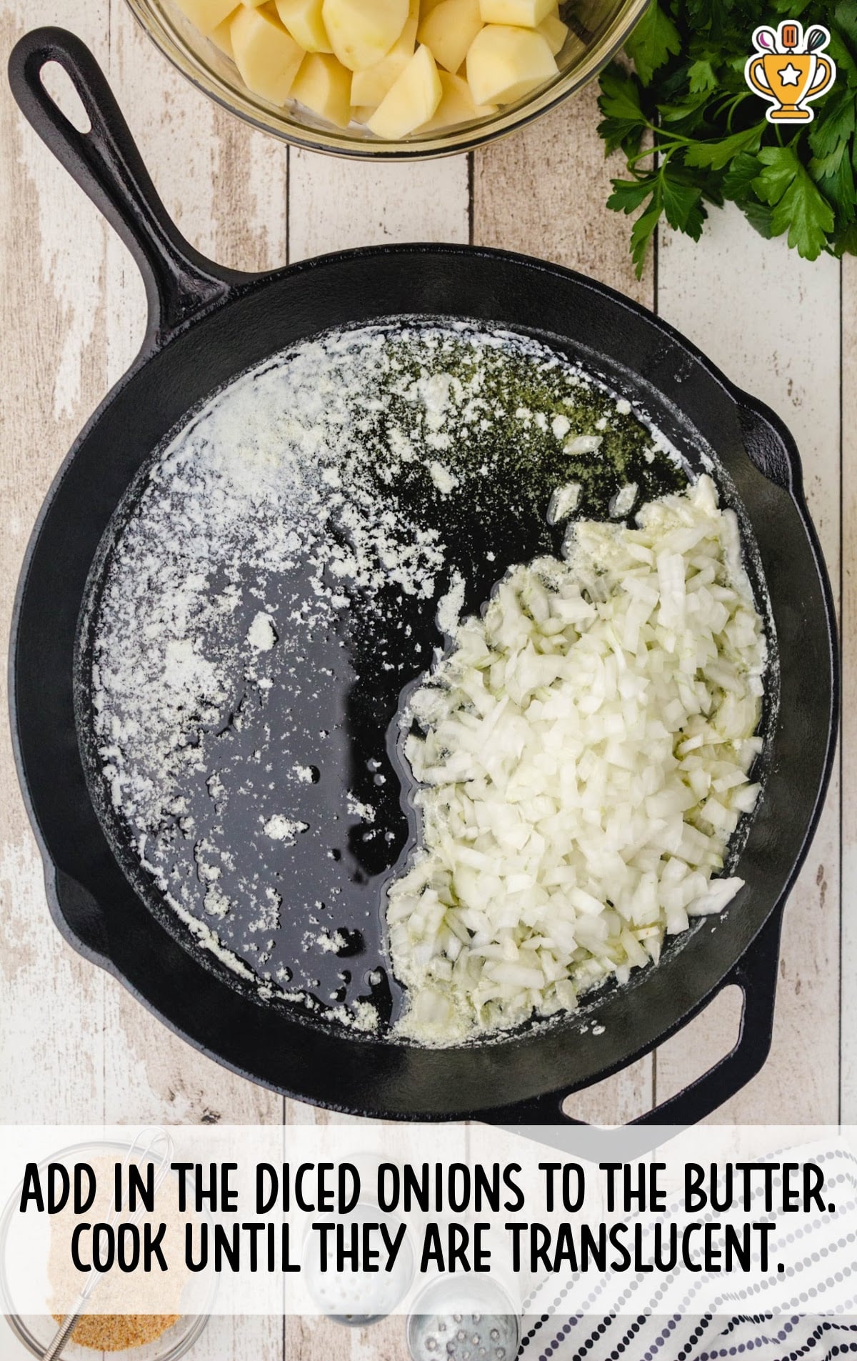 Overhead view of a cast iron skillet with diced onions cooking in melted butter, surrounded by ingredients including chopped potatoes and fresh parsley.
