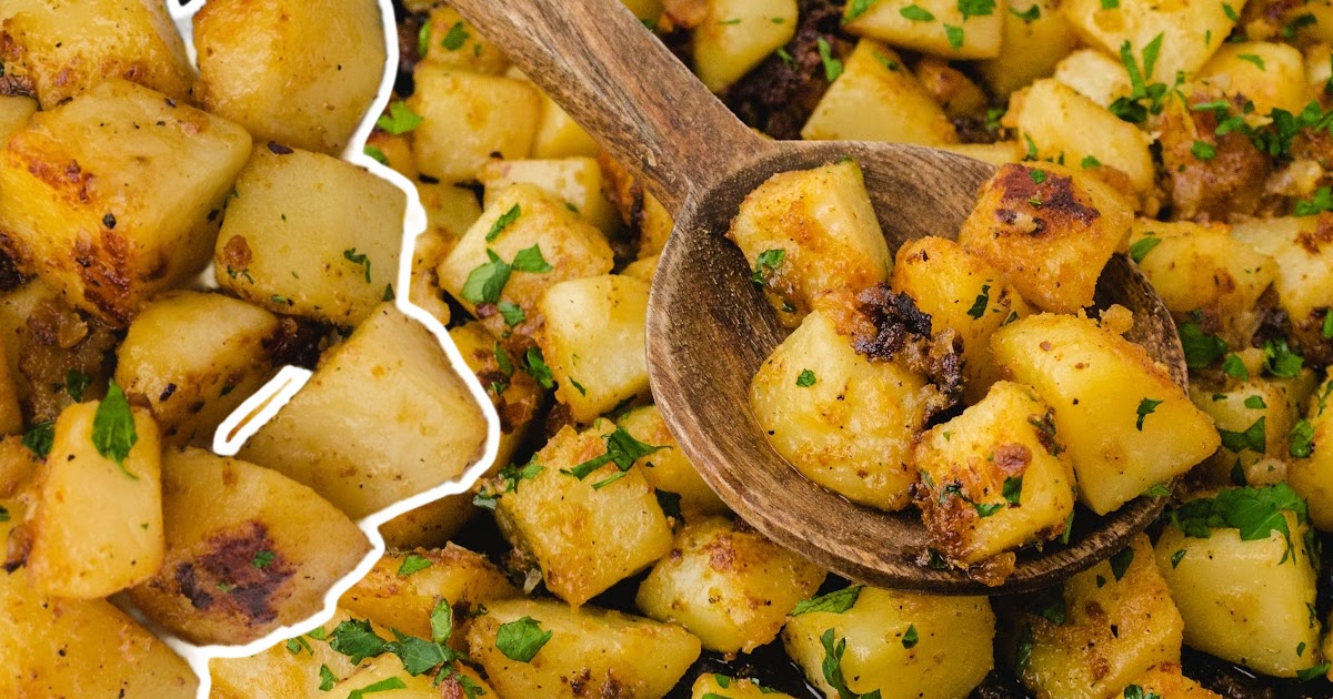 Top-down view of a large spoon lifting crispy, seasoned potatoes from a skillet full of evenly browned, herb-garnished pieces.