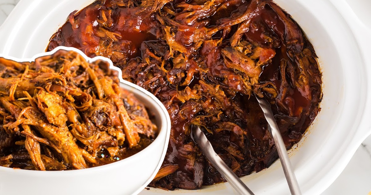 Two-hand held BBQ pulled pork sandwich filled with saucy shredded pork in a golden bun.