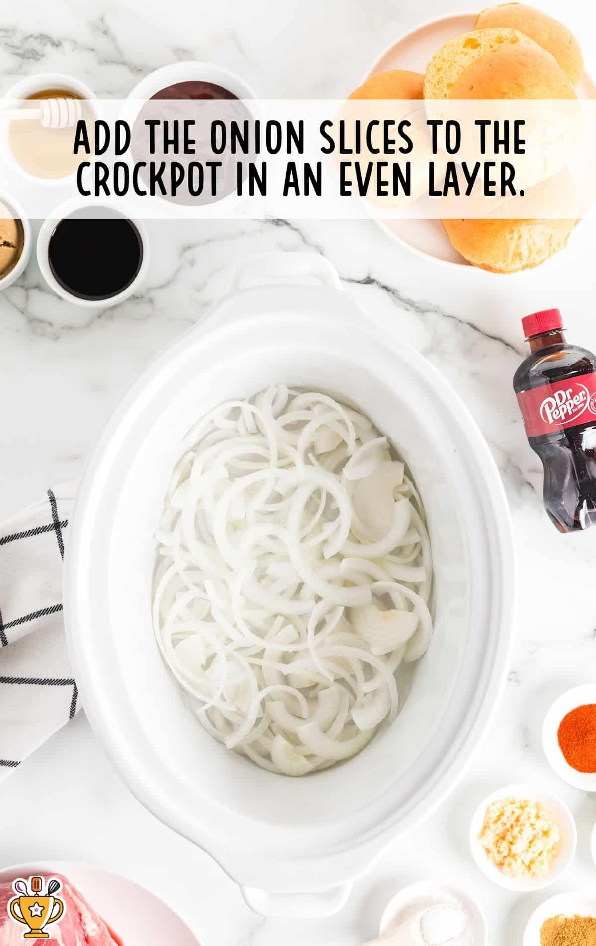 Sliced yellow onions arranged in an even layer inside a white crockpot, ready as the first step in the recipe.