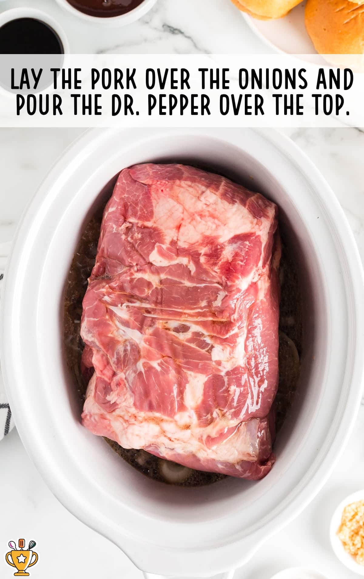 Raw pork butt placed over onions inside the crockpot with Dr. Pepper poured in, beginning the slow cooking process.